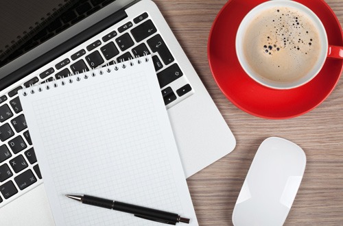 Blank notepad over laptop and coffee cup on office wooden table